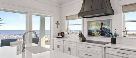 A spacious kitchen with white cabinetry, a large island with a sink, and a view of the ocean through large windows.