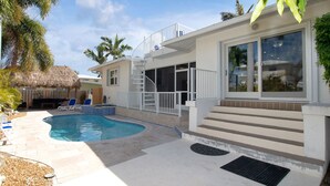 A pool area with a curved pool, lounge chairs, and a staircase leading to a covered deck. - Fisherman's dream!!, Privacy, Heated Pool,Hot Tub, 50' Dockage, Tiki, pets ok,   (Marathon)