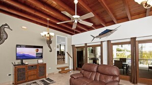A spacious living room with a leather sofa, a flat-screen TV, wooden ceiling beams, and a ceiling fan. - Fisherman's dream!!, Privacy, Heated Pool,Hot Tub, 50' Dockage, Tiki, pets ok,   (Marathon)