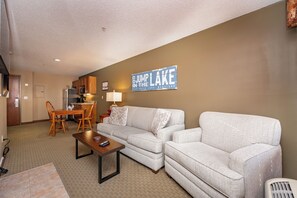 A living room with a sofa, a coffee table, and a dining area with chairs and a table. - Suites at Silver Tree: A116 One Bedroom Standard View (Oakland)