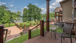 A wooden deck with a view of a lake, a stone building, and a covered area with a table and chairs. - Suites at Silver Tree: A117 One Bedroom Lake View (Oakland)