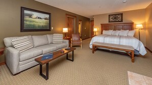 Habitación de hotel con cama, sofá, sillón, una mesita y un cuadro en la pared.