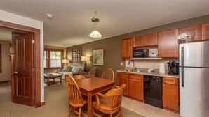 A kitchen with wooden cabinets, a stainless steel refrigerator, and a dining area with a wooden table and chairs.