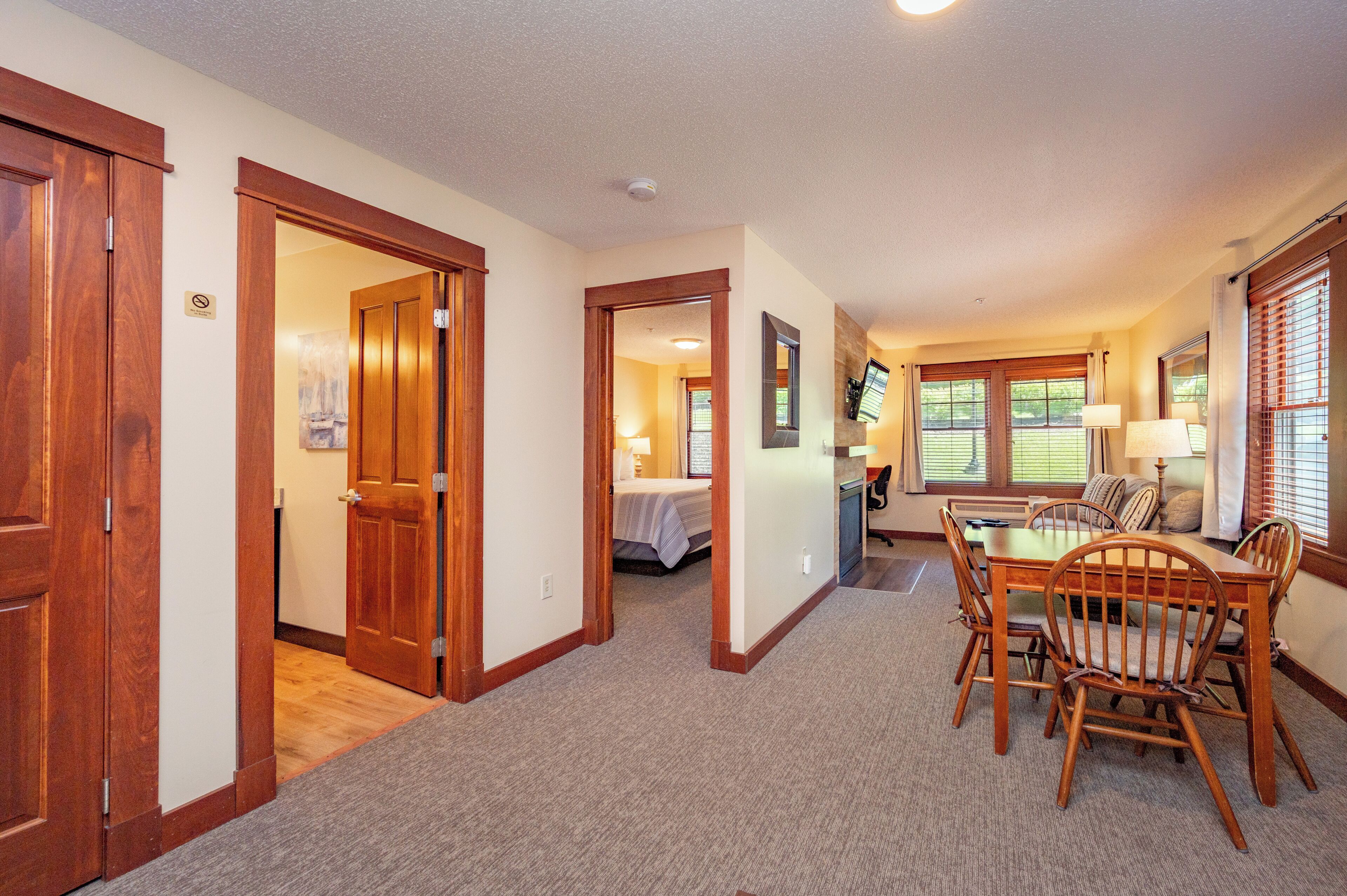 A hotel room with a wooden dining table, chairs, a bed, and a bathroom visible through an open door.