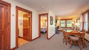 A hotel room with a wooden dining table, chairs, a bed, and a bathroom visible through an open door.