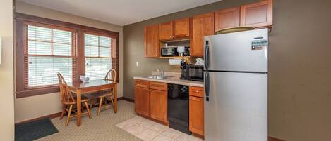 A compact kitchen with wooden cabinets, a stainless steel refrigerator, a microwave, and a dishwasher.