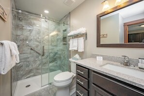 Een moderne badkamer met een douchecabine van glas, een wit toilet en een wastafel met een granieten blad.