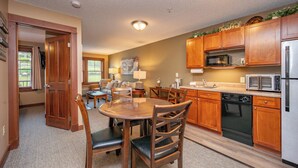A kitchen with wooden cabinets, a microwave, a dishwasher, and a dining area with chairs and a table. - Suites at Silver Tree: A206 One Bedroom Standard View (Oakland)