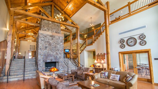 A spacious living area with a stone fireplace, wooden beams, a staircase, and a dining area. - Suites at Silver Tree: A206 One Bedroom Standard View (Oakland)