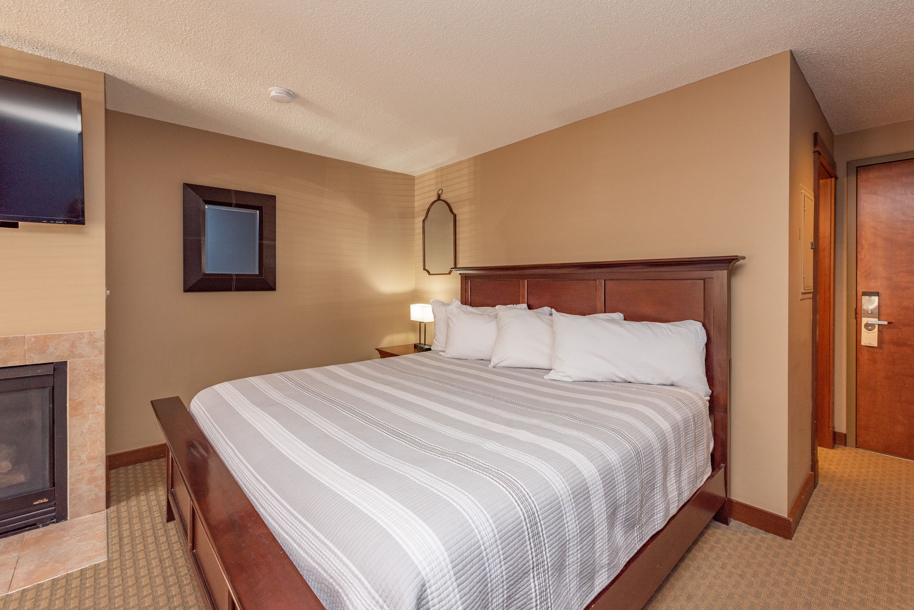 A hotel room with a large bed, a television mounted on the wall, a fireplace, and a door to the right.