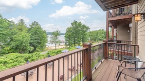 A wooden deck with outdoor furniture overlooking a lake and forest. - Suites at Silver Tree: A213 Studio Lake View (Oakland)