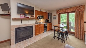 A kitchen with a fireplace, a dining area with a table and chairs, and a view of the outdoors through a sliding glass door. - Suites at Silver Tree: A213 Studio Lake View (Oakland)