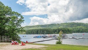 A lakeside view with boats docked, a sandy beach, and a forested hill in the background. - Suites at Silver Tree: A213 Studio Lake View (Oakland)