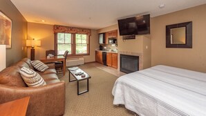 A hotel room with a bed, a sofa, a dining table, a TV, a fireplace, and a kitchen area. - Suites at Silver Tree: A214 Studio Standard View (Oakland)