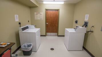A laundry room with two washing machines, a trash bin, and a door with a sign above it.
