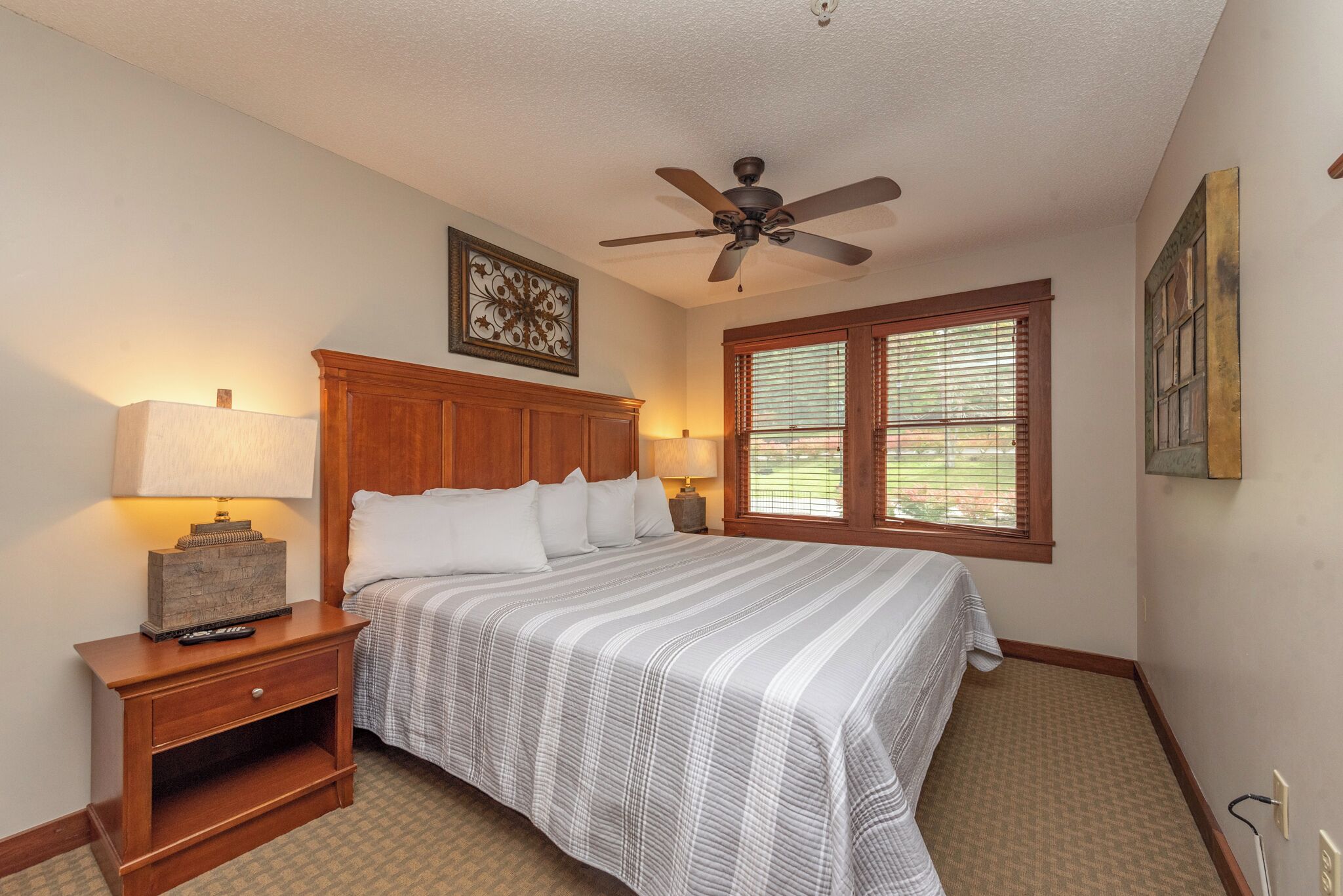 A bedroom with a bed, nightstand, lamp, ceiling fan, and window with blinds.