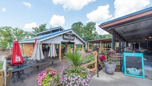An outdoor seating area with tables and umbrellas, a wooden deck, and potted plants. - Suites at Silver Tree: A218 One Bedroom Standard View (Oakland)