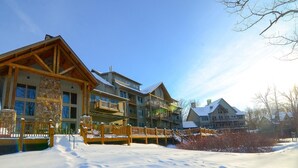 A multi-story lodge with a stone facade, wooden balconies, and a snow-covered ground. - Suites at Silver Tree: A218 One Bedroom Standard View (Oakland)