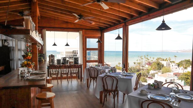 A dining area with tables set for four, wooden chairs, and a view of the ocean. - Suite Leonardo, luxury and comfort close to the malecon. Breakfast included (La Paz)