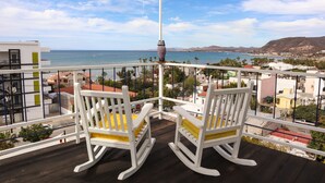 A balcony with two rocking chairs, a view of the sea, and a mountainous landscape in the background. - Suite Leonardo, luxury and comfort close to the malecon. Breakfast included (La Paz)