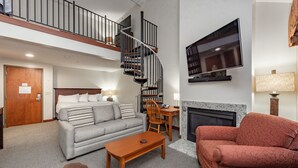 A spacious living area with a grey sofa, a red armchair, a wooden coffee table, and a fireplace. A spiral staircase leads to an upper level. - Suites at Silver Tree: A306 Studio & Loft Standard View (Oakland)