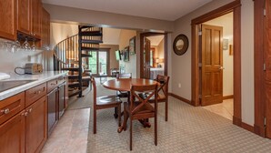 Une cuisine avec des meubles de rangement en bois, une table à manger avec des chaises, un escalier et une porte en bois.