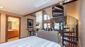 A spacious bedroom with a large bed, a staircase, and a view of the kitchen and living area. - Suites at Silver Tree: A308 Studio & Loft Standard View (Oakland)