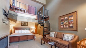 A hotel room with a bed, a sofa, a coffee table, a staircase, and a framed artwork on the wall. - Suites at Silver Tree: A310 Studio & Loft Standard View (Oakland)