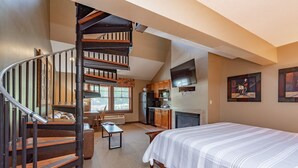 A bedroom with a large bed, a wooden staircase, a kitchen area, and a living space. - Suites at Silver Tree: A310 Studio & Loft Standard View (Oakland)