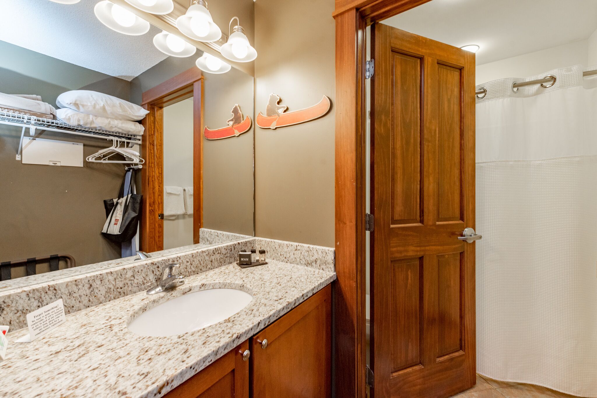 A bathroom with a double sink, wooden door, and a mirror with a canoe decoration.