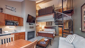 A modern living room with a dining area, a fireplace, a large bed, and a staircase leading to an upper level. - Suites at Silver Tree: A314 Studio & Loft Standard View (Oakland)