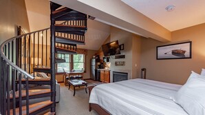A bedroom with a large bed, a wooden staircase, a fireplace, and a kitchen area. - Suites at Silver Tree: A314 Studio & Loft Standard View (Oakland)
