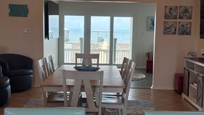 A dining area with a table and chairs, a view of the ocean through a sliding glass door, and a beach visible outside. - 4BR/3BA with Private Beach, Pier/Boat Lift, Dog Friendly, Free Kayaks, Best WiFi (Dauphin Island)