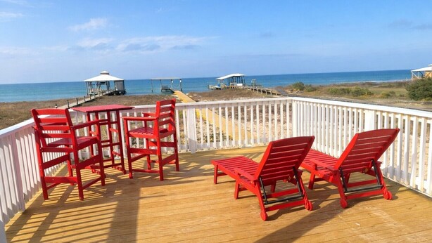 A wooden deck with red chairs and tables overlooking the beach. - 4BR/3BA with Private Beach, Pier/Boat Lift, Dog Friendly, Free Kayaks, Best WiFi (Dauphin Island)