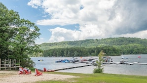 A lakeside view with boats docked, a sandy beach, and a forested hill in the background. - Suites at Silver Tree: A316 Studio & Loft Standard View (Oakland)