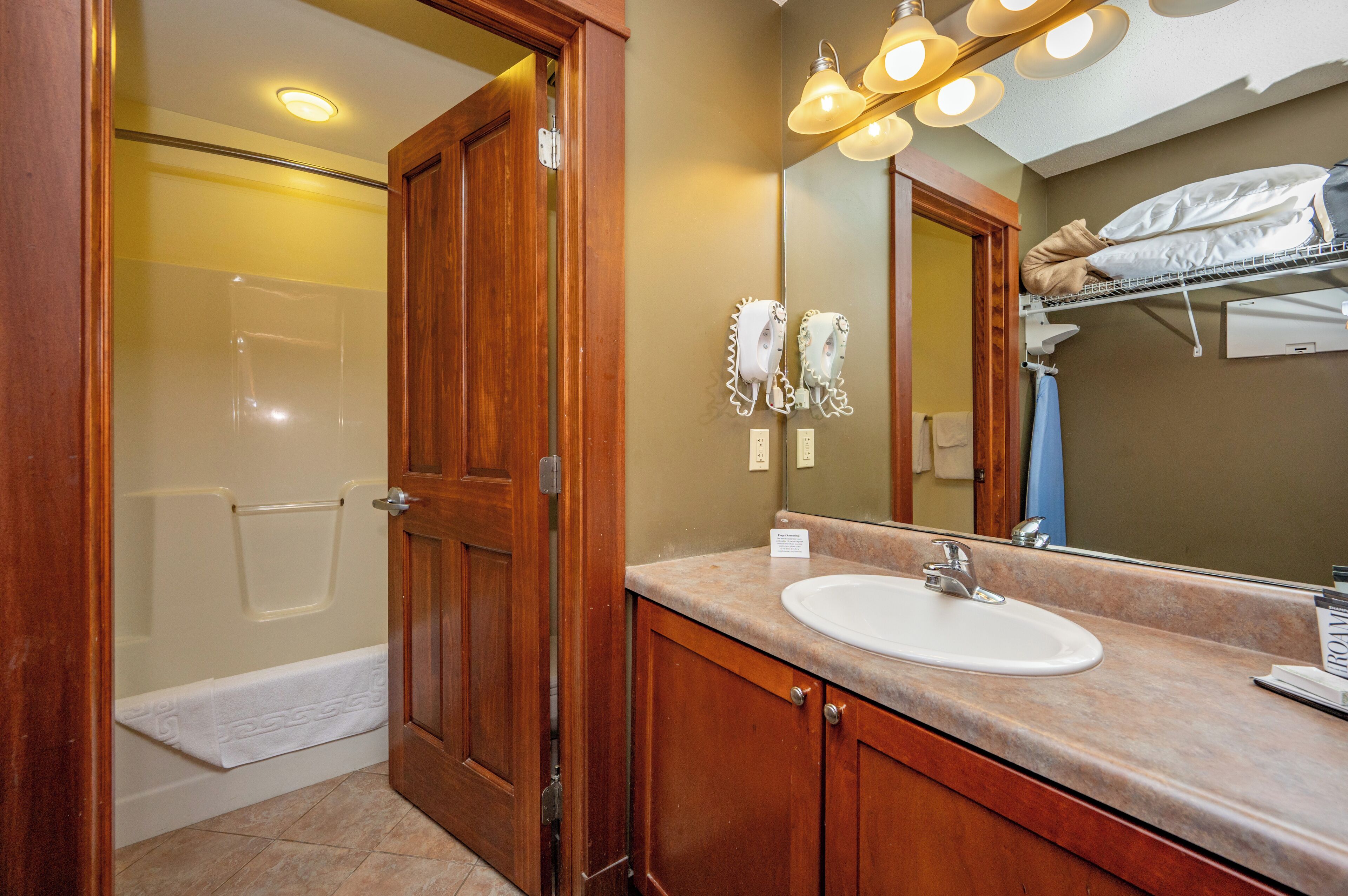 A bathroom with a wooden door, a white sink, and a mirror with lights.