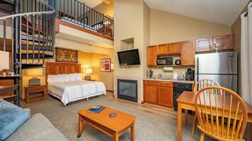 A hotel room with a bed, a desk, a chair, a television, a kitchen area with a microwave, a refrigerator, and a staircase.
