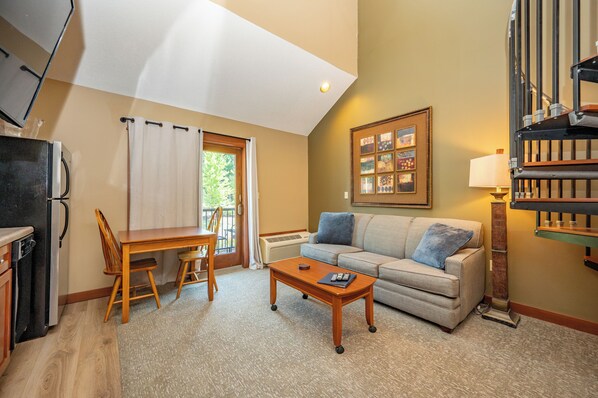 A living room with a sofa, a coffee table, a dining table with chairs, a radiator, and a framed picture on the wall. - Suites at Silver Tree: A316 Studio & Loft Standard View (Oakland)