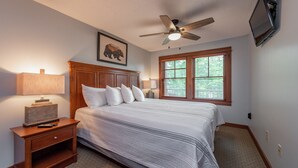 Ein Schlafzimmer mit Bett, Nachttisch, Lampe, Deckenventilator und einem Wand-Fernseher.
