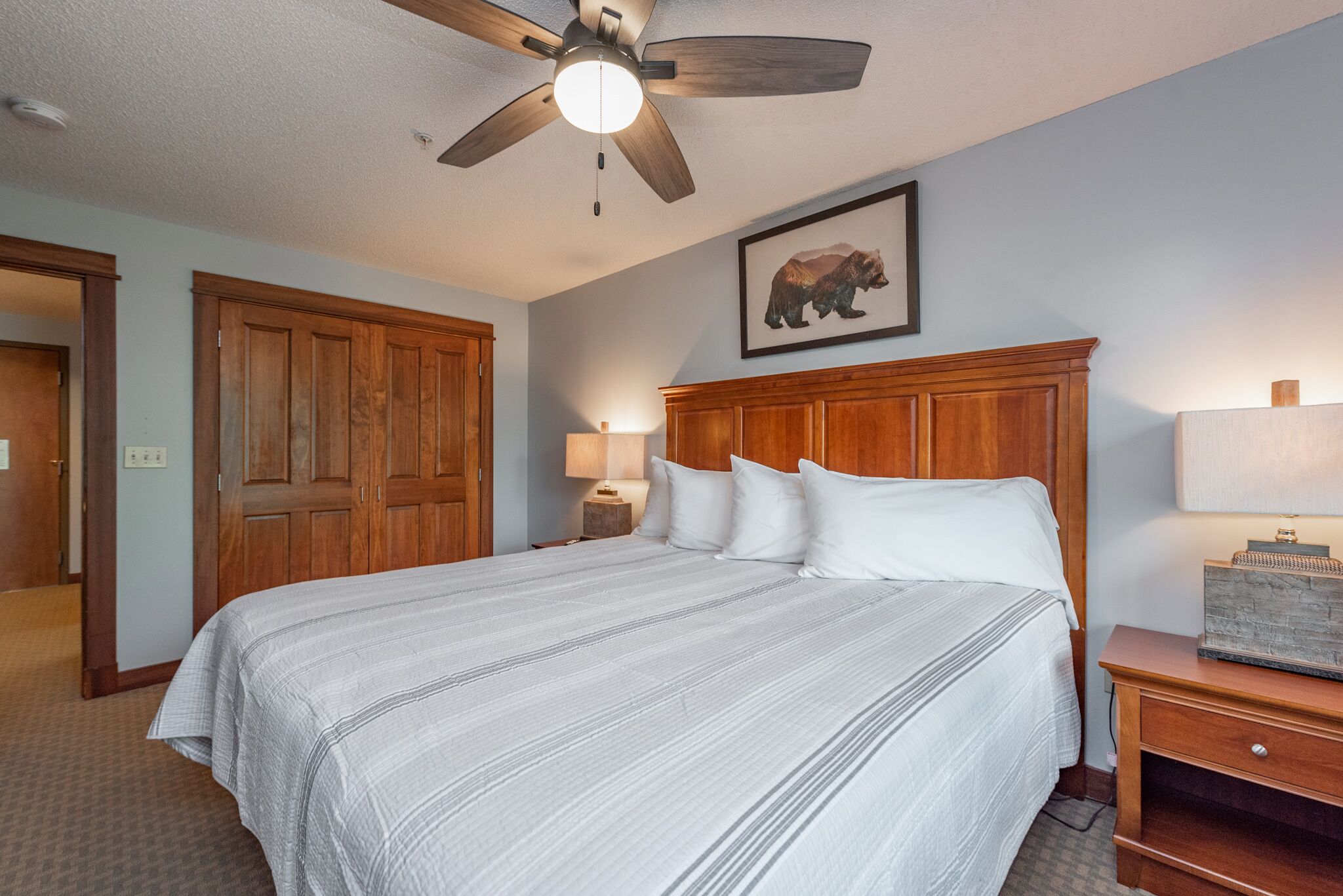 A bedroom with a large bed, wooden headboard, a ceiling fan, and a framed picture of a bear on the wall.
