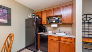 A compact kitchen with wooden cabinets, a black refrigerator, a microwave, and a dishwasher. - Suites at Silver Tree: B106 One Bedroom Standard View (Oakland)
