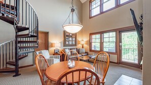 A spacious living area with a wooden dining table, comfortable seating, a staircase, and large windows providing natural light. - Suites at Silver Tree: B203 One Bedroom & Loft Lake View (Oakland)