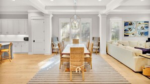 A spacious living area with a dining table, wicker chairs, a sofa, and a large abstract painting on the wall.