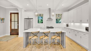 A modern kitchen with white cabinetry, a large island with bar stools, stainless steel appliances, and pendant lighting.