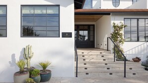 Un edificio moderno con fachada blanca, grandes ventanales y una escalera de piedra que lleva a una puerta de madera.