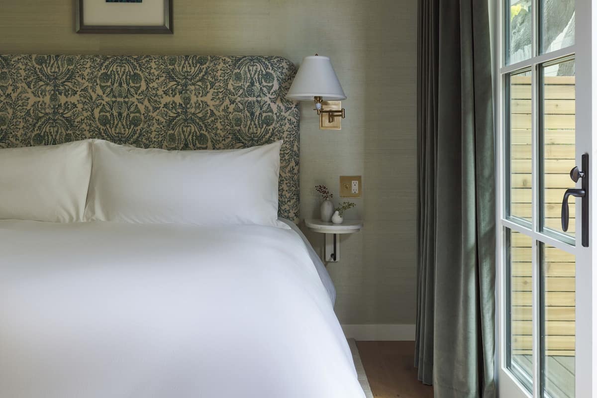 A neatly made bed with a patterned headboard, a bedside table with a lamp, and a window with curtains.