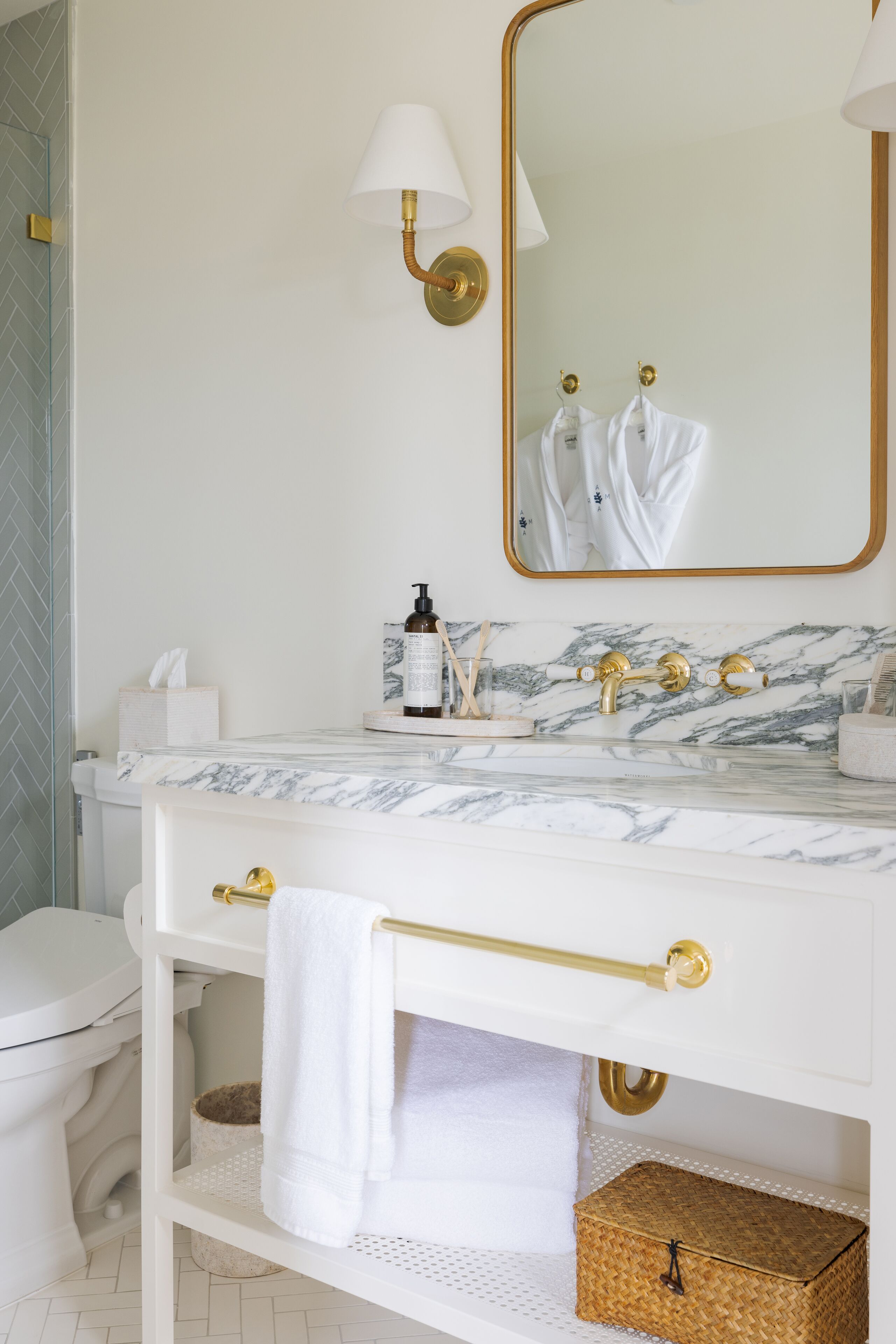 A bathroom with a white toilet, marble sink, gold fixtures, a mirror, and a towel rack.