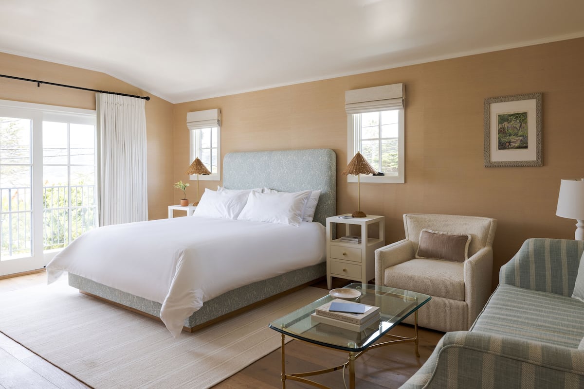 A bedroom with a large bed, a glass coffee table, a chair, and a nightstand with a lamp.