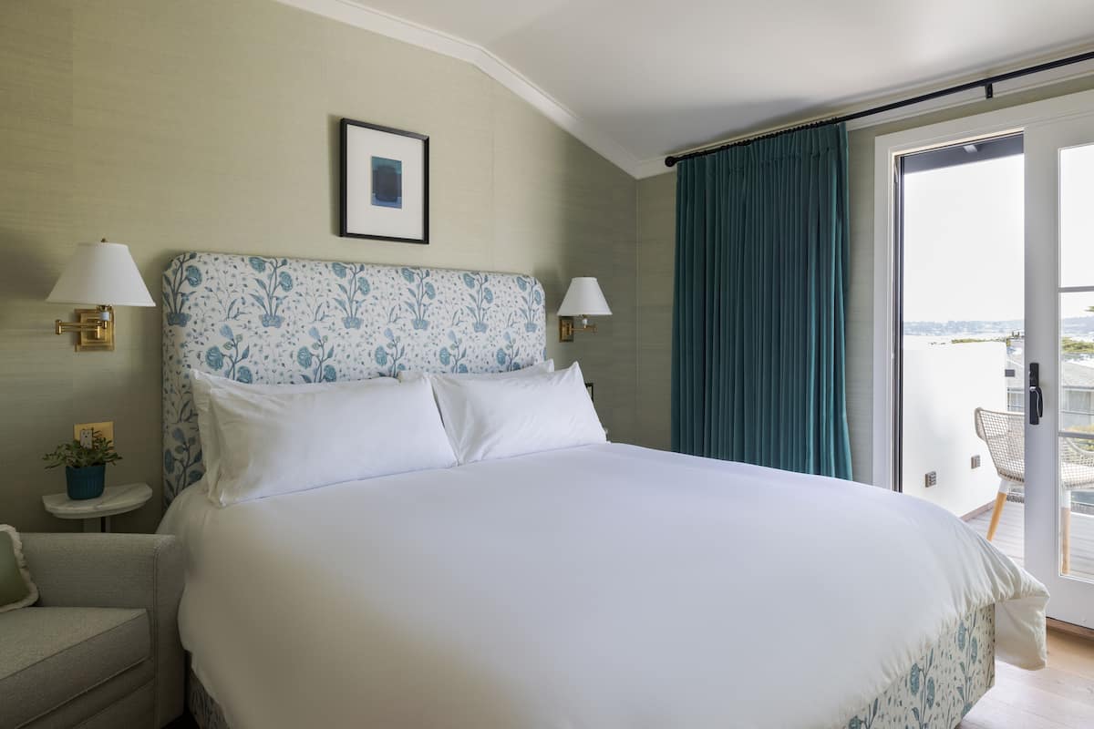 A hotel room with a large bed, two bedside lamps, a framed picture on the wall, and a view through a sliding door.