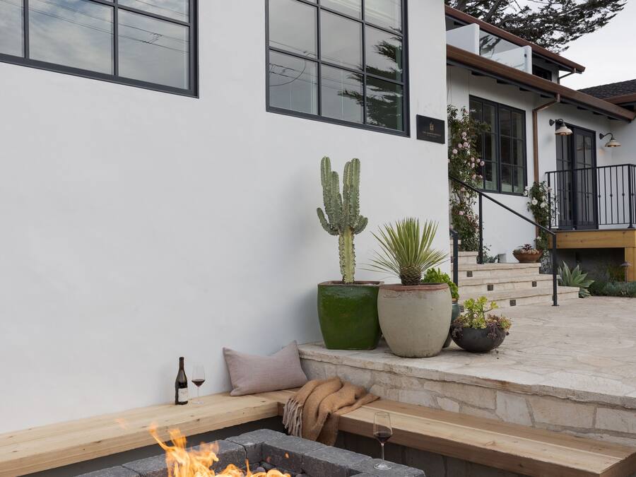 A modern house with a fire pit, potted plants, and a bench.